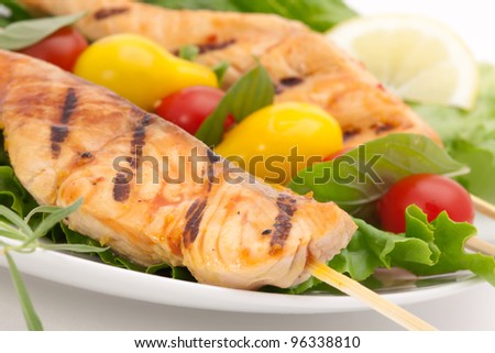 Closeup of grilled salmon on bamboo sticks and vegetable skewers with fresh tarragon and green salad