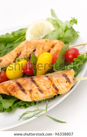 Closeup of grilled salmon on bamboo sticks and vegetable skewers with fresh tarragon and green salad