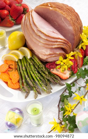 Table set with festive glazed ham for Easter celebration dinner garnished with asparagus, carrots, strawberry, and lemon wedges.