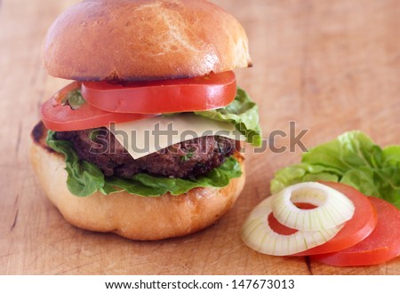 Hamburger with a juicy beef patty, fresh lettuce, onion and fresh bun standing on brown paper on a wooden tabletop