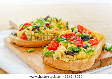 Scrambled eggs with tomato olives onion and parsley served on toast bread
