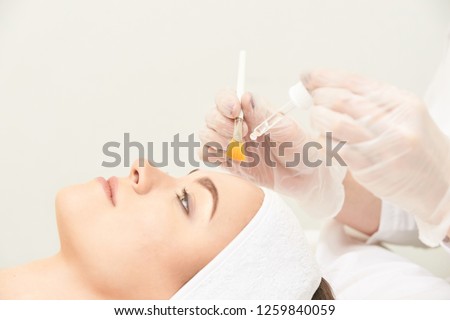 Young woman cleaning face skin in salon. Retinol peel with brush. Acid organic peeling.