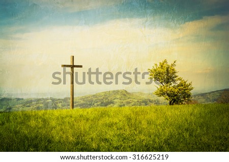 A cross on a green mountain meadow with clouded sky behind.