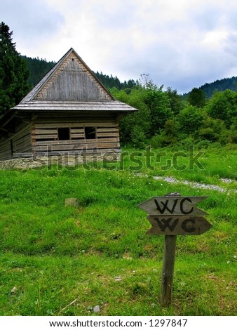 A funny road sign in front of an unfinished wooden cottage in the mountains.
