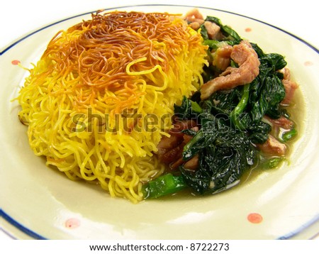 Closeup of a dish of Chinese fried noodles with green vegetable and ham on a ceramic plate