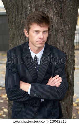 Man leaning against tree in city, arms crossed