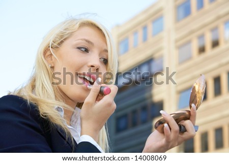 Businesswoman applying lipstick outdoors in city
