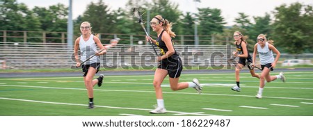 Opposing teams doing battle during a girls Lacrosse game, outdoors on playing field.