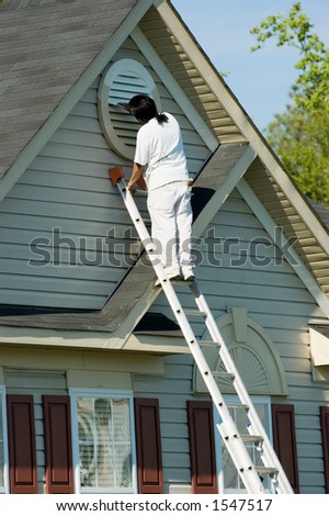 Painter working atop an extension ladder on a two-story suburban home.