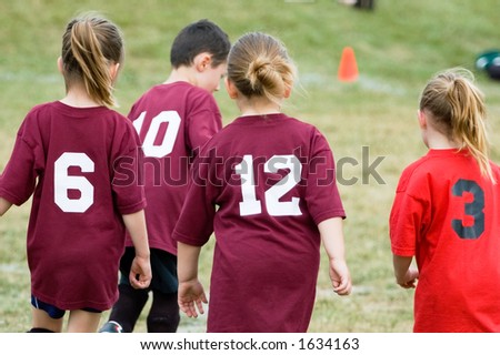 Three girls chasing a boy during a youth soccer league game.