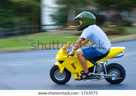 Boy speeds through a turn on a motorized dirt bike. Panning blur technique freezes the motorcycle against a motion filled background.