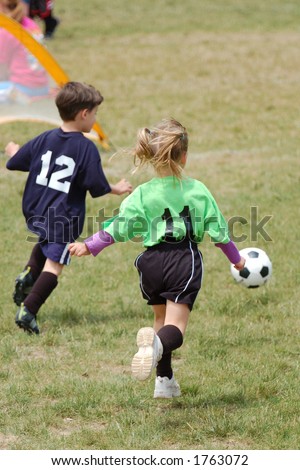 Young boy and girl race for the ball during a youth soccer game. Slight DOF focus on girl player in green.