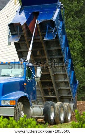 Dump truck on a residential building lot dumping a load of topsoil. Interesting view of the underside of the truck bed and bright blue color.
