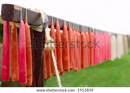 Colorful hand dipped candles cooling outdoors on a wooden rack. Whited out sky provides room for text.