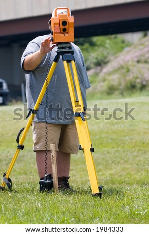 Land surveyor looking through and operating an electronic distance meter atop a tripod.