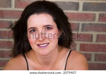Portrait of a young woman, brick wall in the background. Woman is wearing make-up and image is styled after fashion photography.