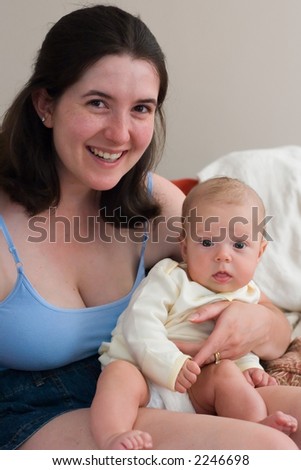 Young baby sits on her moms lap. Both smile for the camera.