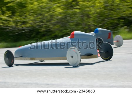 Two soap box race cars speed down the track. Panning blur captures sense of speed and slow shutter allows spinning tires show rotation as well.