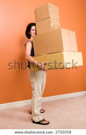 A young woman looks out from behind a tall stack of cardboard boxes she is carrying. Image suggests a moving day or shipping/retail themes.