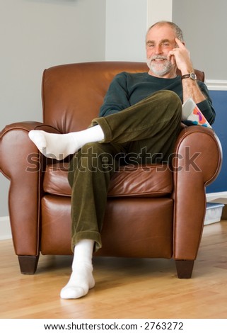 Cheerful older gentleman sitting and relaxing in a leather chair. Leaning head on hand or pointing to head.