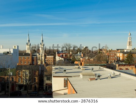 View of church spires and rows of historic brick buildings in classic rural American town. Captured during late afternoon, giving golden hue and long shadows.