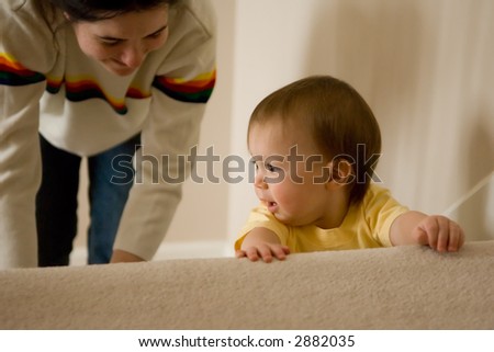Young baby girl playing on the stairs, mother is near by helping her learn to climb the stairs safely. Lifestyle image.
