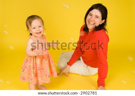 Mother and daughter looking cheerful and full of life, spring portrait against yellow background. Real bubbles adding fun and interest.