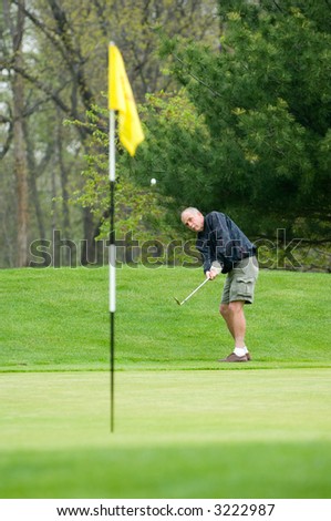 Gentleman making chip shot from the fringe of the green. Ball is in mid-air with some motion blur. Man\'s eyes are intensely following the ball after taking his shot.