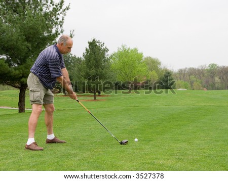 Golfer adjusts his stance as he is about to tee off. First of series, later in sequence ball can be seen flying off the tee.