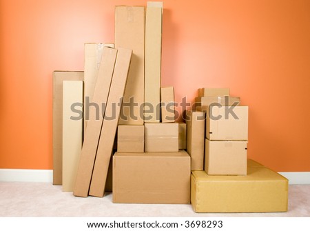 Large pile of boxes stacked against the wall of an empty room. Themes of moving in or moving out, or of many retail boxes of a shipment that has just arrived or is ready to ship out.
