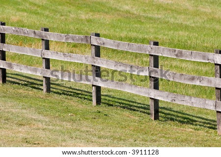Five wooden posts anchor a three rail wooden fence which lines a pasture.