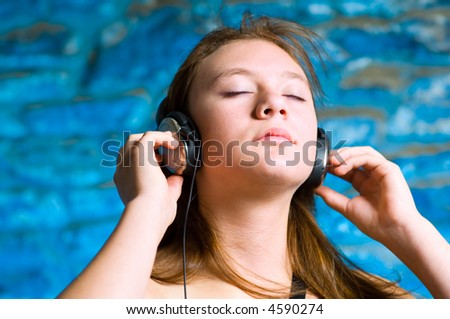 Young teen girl deeply feeling the music. Urban stone wall background with blue gel backlight for effect. Moderately shallow DOF focus on hands and eyes.