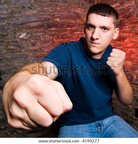 Extreme close-up of a fist, captured with a fisheye lens to deliver the knock-out punch proportion. Urban setting with rock wall. Focus on the punching fist.