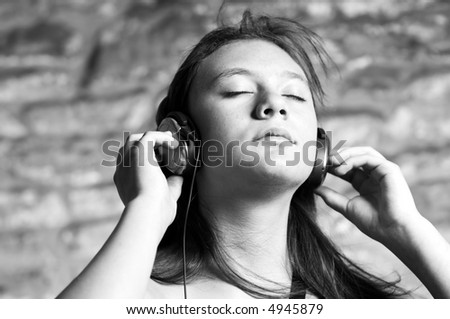 Young teen girl deeply feeling the music. Urban stone wall defocused in background. Moderately shallow DOF focus on hands and eyes. Carefully converted to black and white.