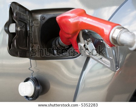 Bright red gas pump inserted into an automobile gasoline tank. NOTE: Metallic fleck to the paint on the car not to be confused with noise, it is texture in the paint at varying focal distance.