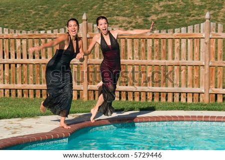 Two young women in formal dresses running and jumping into a pool. Focus on models faces, some motion blur in extremities.