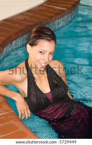 Beautiful young brunette woman in a swimming pool with fancy dress on. Was she thrown in? Too hot and without a swimsuit?