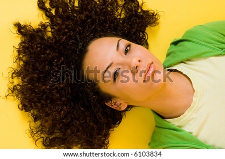 Intelligent and direct eye contact from a beautiful young model. Hair fanned out on bright yellow background for a fashion look.