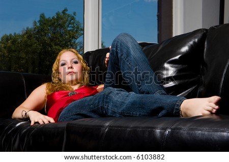 Young woman with red hair and bright red top reclining on a black leather couch.
