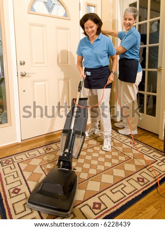 Two house keeping maids working in a high end entry way to a residential home. One made using a vacuum cleaner.
