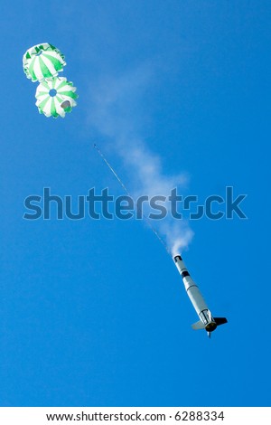 Challenging shot of a model rocket which has just deployed it\'s twin parachutes. Smoke from the ejection charge still billowing out of the body. Captured with long range zoom while rocket descending.
