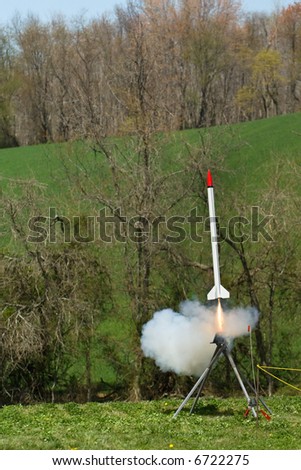 Model rocket launches off the launchpad with copious amounts of smoke and flame emitting from its engine.