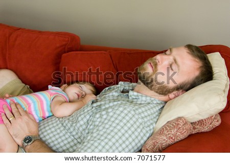 Slice of life image -- father asleep on the sofa with one year old baby daughter. Taken with natural light, shallow depth of field, fathers face partially out of focus with crisp focus on baby\'s face.