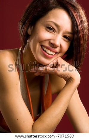 Vibrant and vivacious young woman. Her eyes and smile shine conveying strength, character, and confidence. Deep red background lends an artistic character to the portrait.