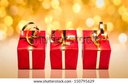 Photo of three red and gold gift boxes with out of focus lights on a golden background