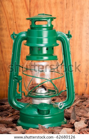 Green lantern on bark chips against wooden background