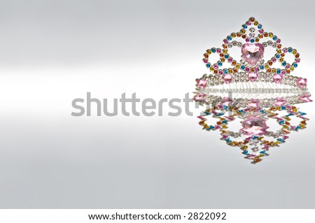 Multi colored tiara isolated on gradient background with water reflection. Copy space to left.