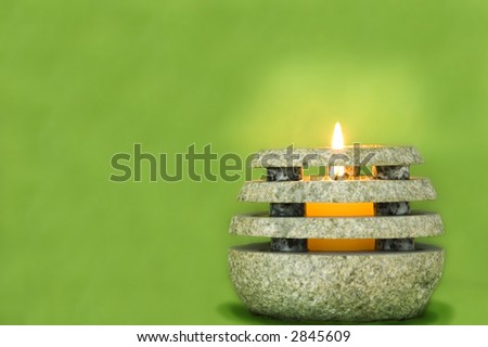 Votive candle burns in stone holder against green background
