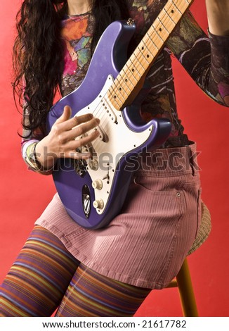 Girl in bright coloured outfit with rainbow stockings holds and plays electric guitar