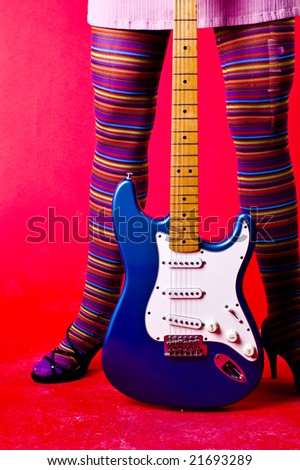 Girl in bright coloured outfit with rainbow stockings holds electric guitar